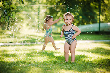 Image showing The two little baby girls playing with garden sprinkler.