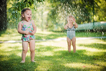 Image showing The two little baby girls playing with garden sprinkler.