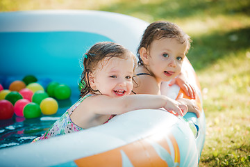 Image showing The two little baby girls playing with toys in inflatable pool in the summer sunny day