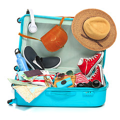 Image showing The open blue suitcase, sneakers, clothing, hat, and retro camera on white background.