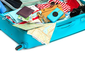 Image showing The open blue suitcase, sneakers, clothing, hat, and retro camera on white background.