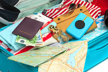 Image showing The open blue suitcase, sneakers, clothing, hat, and retro camera on white background.