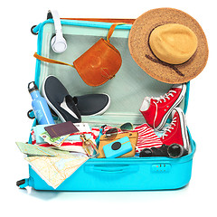 Image showing The open blue suitcase, sneakers, clothing, hat, and retro camera on white background.