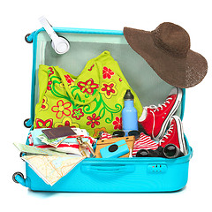 Image showing The open blue suitcase, sneakers, clothing, hat, and retro camera on white background.