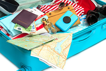 Image showing The open blue suitcase, sneakers, clothing, hat, and retro camera on white background.