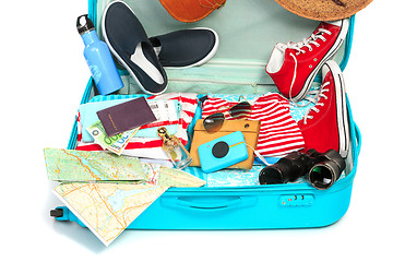 Image showing The open blue suitcase, sneakers, clothing, hat, and retro camera on white background.