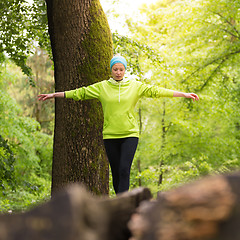 Image showing Woman holding balance on tree trunk in nature.