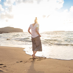 Image showing Woman walking on sand beach at golden hour