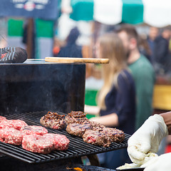 Image showing Beef burgers being grilled on food stall grill.