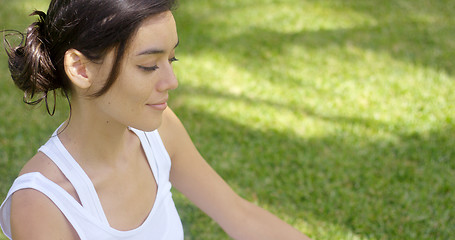 Image showing Serene young woman meditating on a green lawn