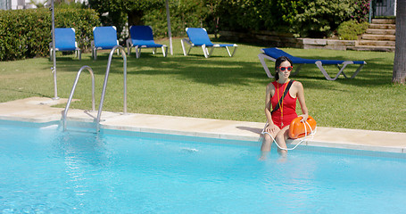 Image showing Lifeguard in red swimsuit sitting at edge of pool