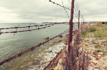 Image showing barb wire fence over gray sky and sea