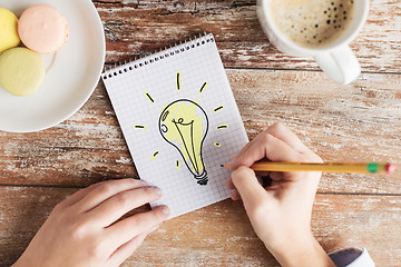 Image showing close up of hands drawing bulb to notebook