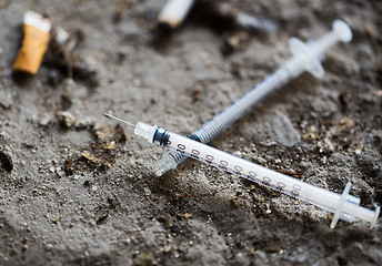 Image showing close up of syringe and smoked cigarette on ground