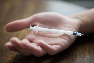 Image showing close up of addict hand and used drug syringe