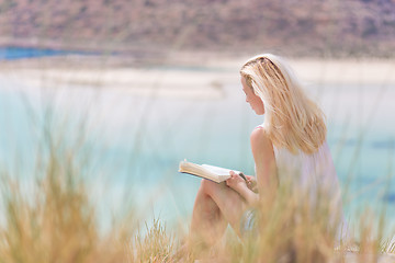 Image showing Woman reading book, enjoying sun on beach.