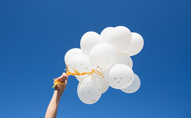 Image showing close up of hand with white balloons in blue sky