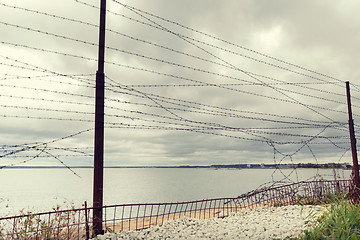 Image showing barb wire fence over gray sky and sea