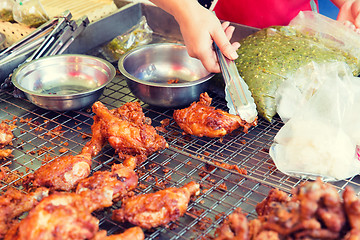 Image showing close up of cook hand with tongs grilling chicken