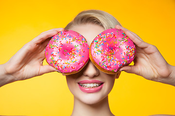 Image showing Short-haired model covering eyes behind two pink donuts