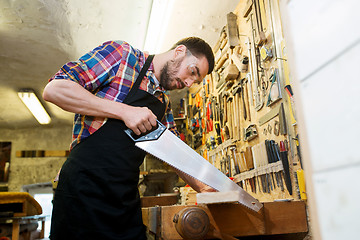 Image showing carpenter working with saw and wood at workshop