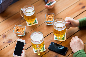 Image showing close up of hands with smartphones and beer at bar