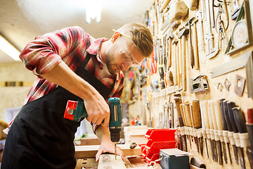 Image showing carpenter with drill drilling plank at workshop