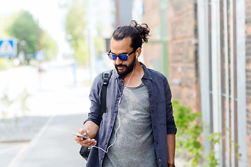 Image showing man with earphones and smartphone walking in city