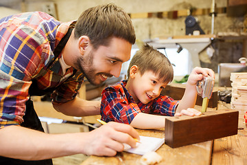 Image showing dad and son with ruler measuring plank at workshop