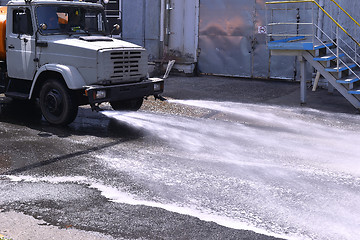 Image showing Water truck watering the asphalt at a manufacturing plant for du