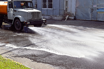 Image showing Water truck watering the asphalt at a manufacturing plant for dust suppression