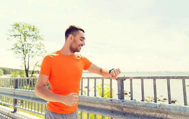 Image showing smiling young man with smart wristwatch at seaside