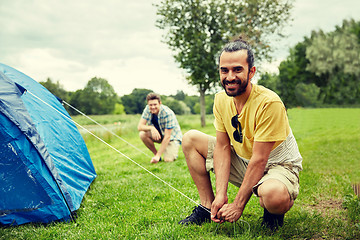 Image showing smiling friends setting up tent outdoors