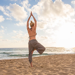 Image showing Woman practicing yoga on sea beach at sunset.