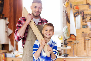 Image showing happy father and son with wood plank at workshop