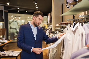 Image showing happy young man choosing clothes in clothing store