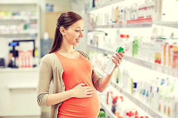 Image showing happy pregnant woman choosing lotion at pharmacy