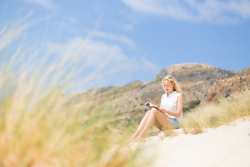 Image showing Woman reading book, enjoying sun on beach.