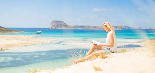 Image showing Woman reading book, enjoying sun on beach.