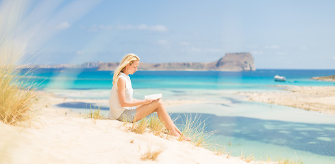 Image showing Woman reading book, enjoying sun on beach.