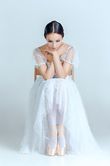 Image showing Professional ballerina sitting with her ballet shoes on the gray background