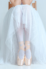 Image showing Professional ballerina sitting with her ballet shoes on the gray background
