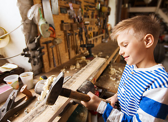 Image showing happy little boy with hammer and plank at workshop