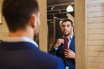 Image showing man trying tie on at mirror in clothing store