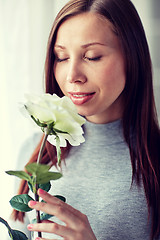 Image showing happy woman smelling big white rose at home