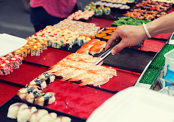 Image showing close up of hand with tongs taking sushi