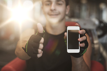 Image showing young man with smartphone showing thumbs up in gym