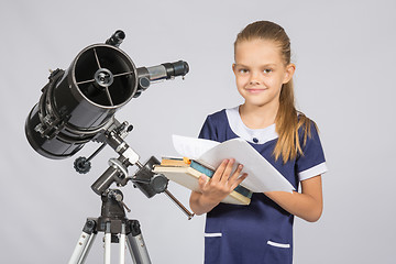 Image showing Schoolgirl astronomer leafing through books standing at the telescope