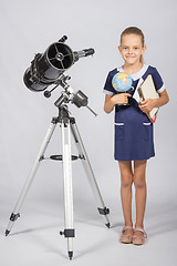 Image showing Schoolgirl astronomer is a telescope with a globe and books in the hands