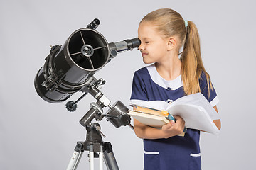 Image showing School girl looking through a telescope standing with textbooks